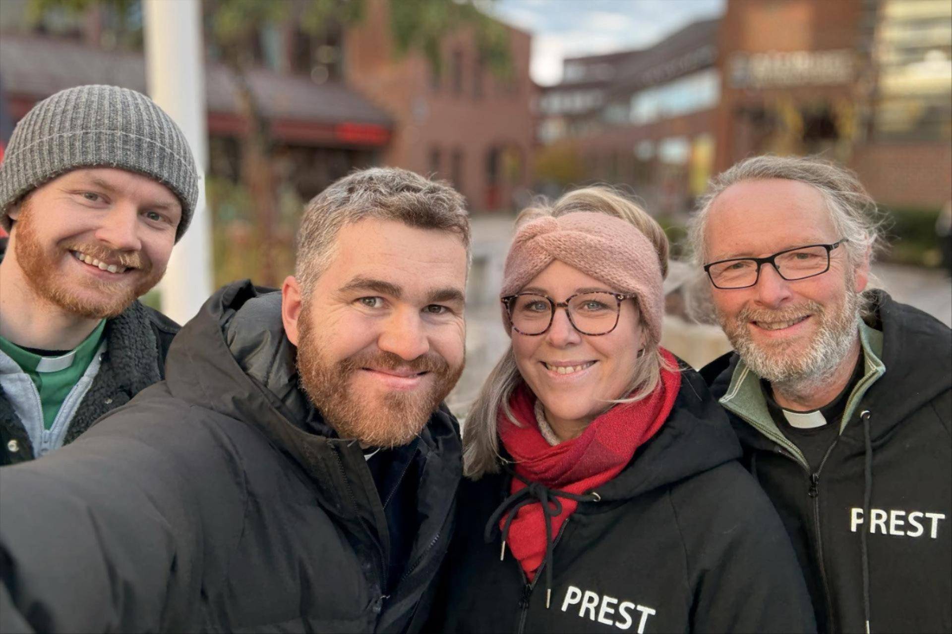 Bide av en diakon og tre prester på stand, de smiler i kamera. 